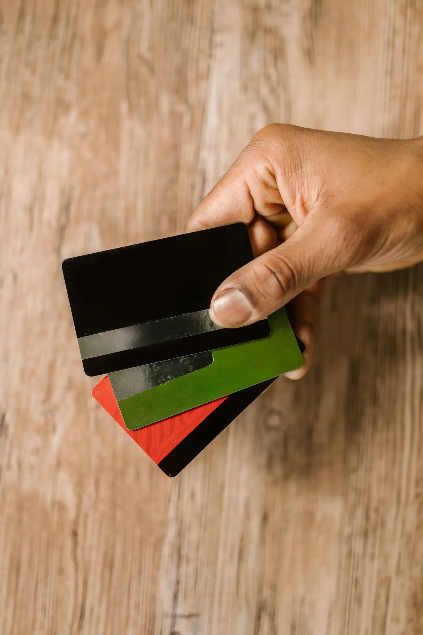 يد تحمل عدة بطاقات بنكية فوق طاولة خشبية