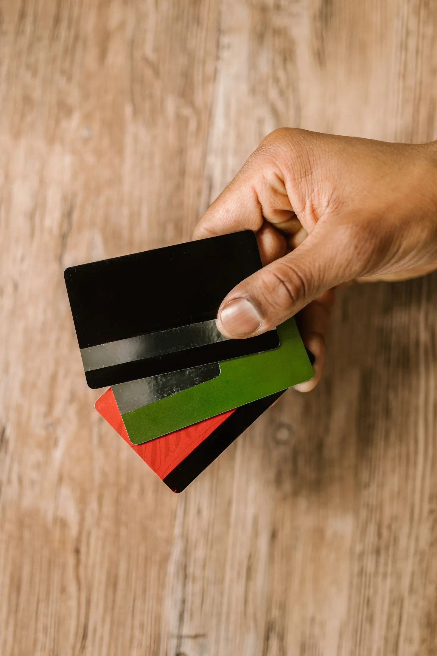 يد تحمل عدة بطاقات بنكية فوق طاولة خشبية
