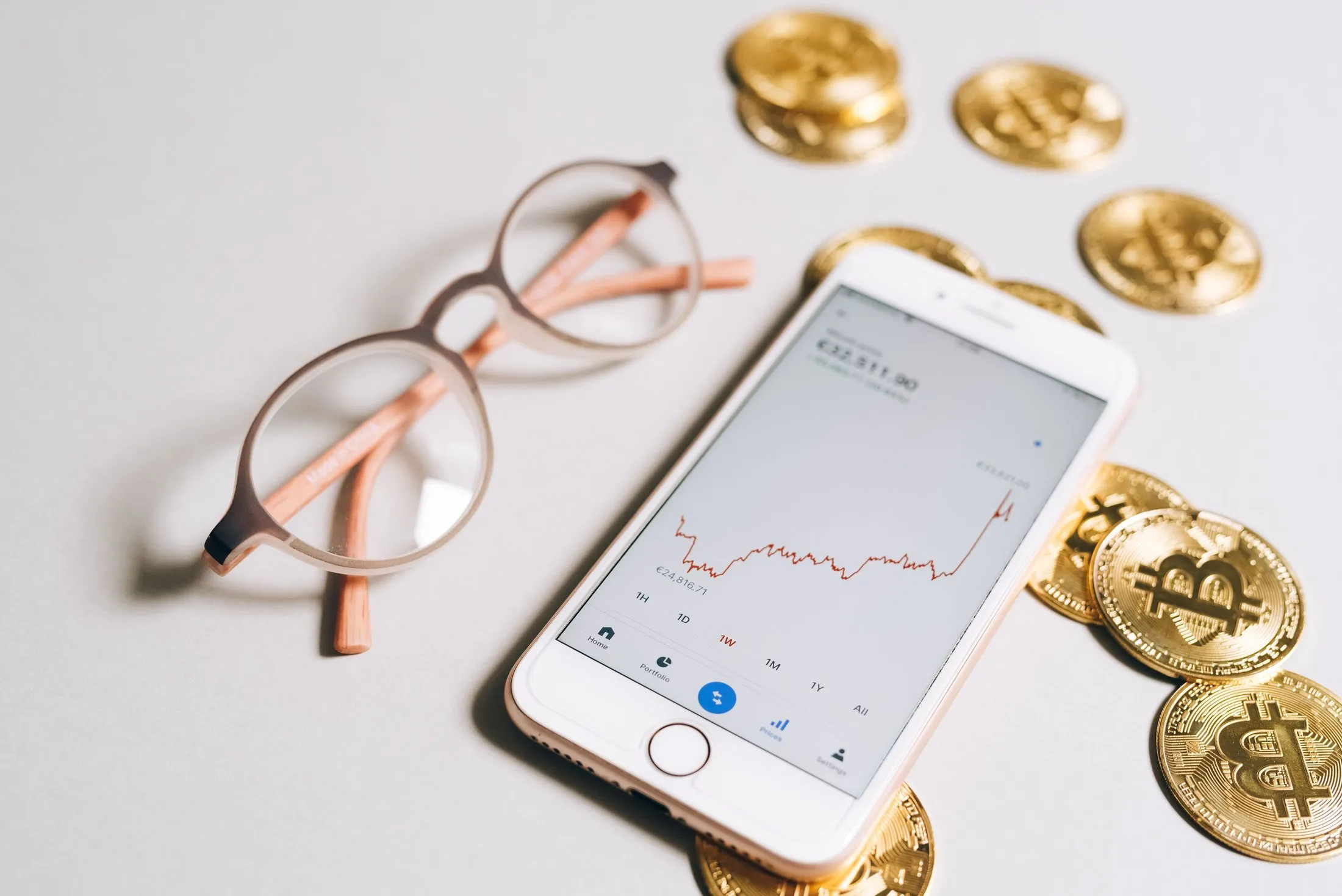تطبيق تداول يعرض رسماً لبيتكوين على هاتف تحيط به عملات ذهبية